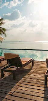 The image shows a sunny deck with lounge chairs and umbrellas overlooking a calm ocean and a clear sky.