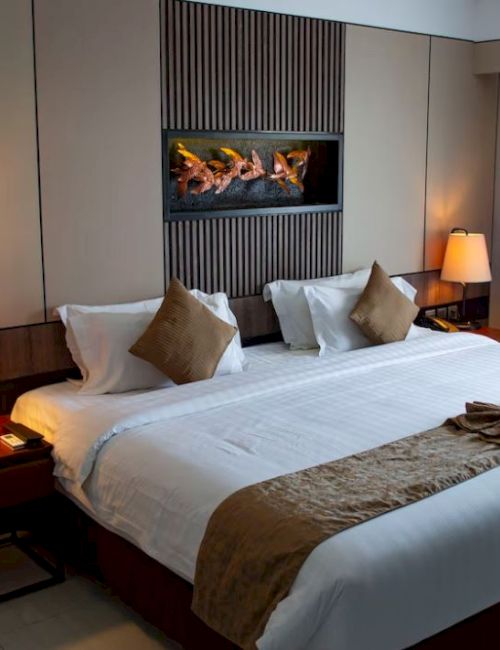 The image shows a hotel room with a neatly made king-size bed, bedside tables with lamps, and a decorative wall art above the bed.