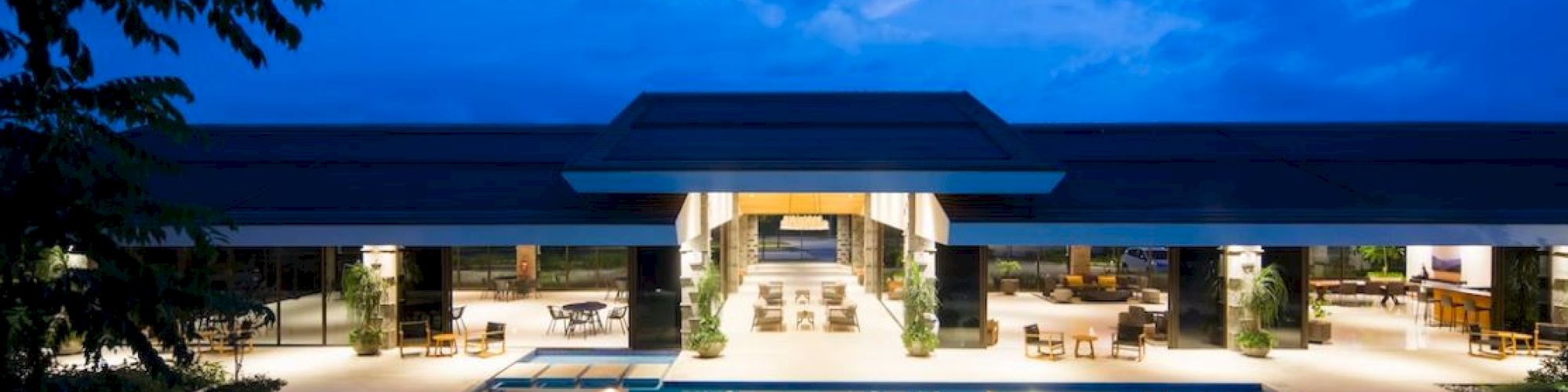 A luxurious poolside area at night, with modern architecture, ambient lighting, and a reflective water surface under a deep blue sky.