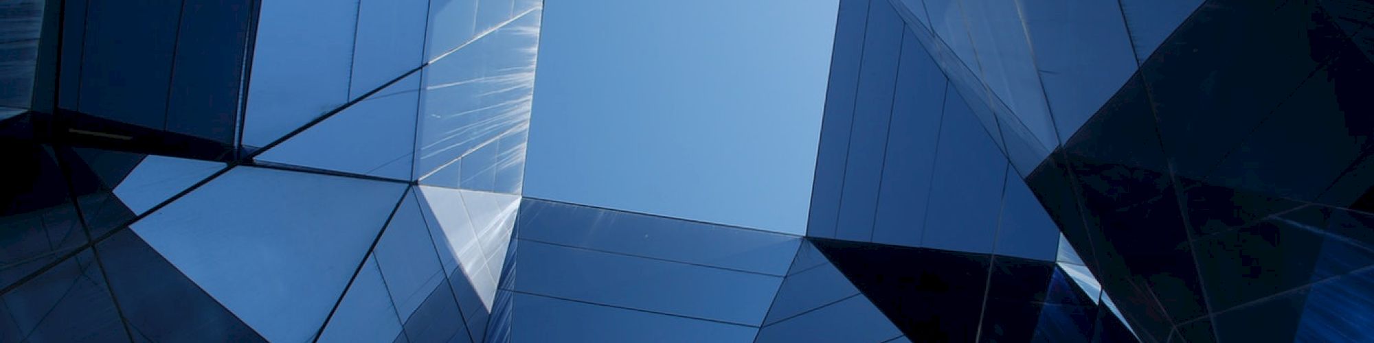 The image shows an abstract view of reflective glass structures creating geometric shapes against a blue sky.