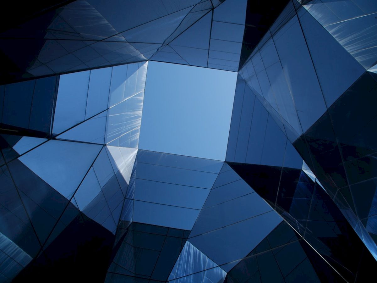 The image shows an abstract architectural design with reflective glass surfaces forming a geometric pattern, creating a visual tunnel effect.