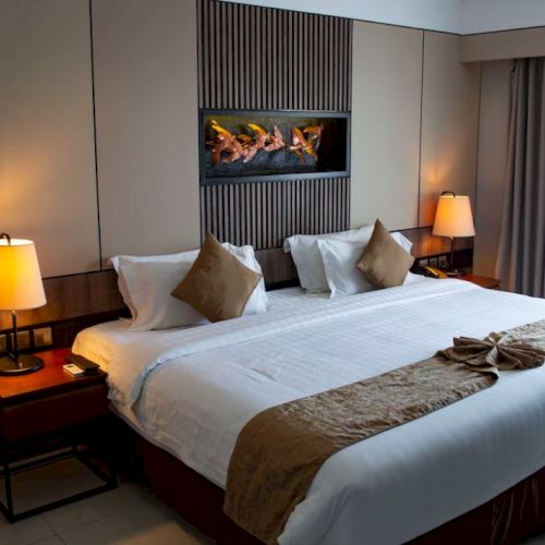 A well-lit hotel room with a large bed, lamps on nightstands, and a decorative wall feature, creating a cozy and inviting atmosphere.