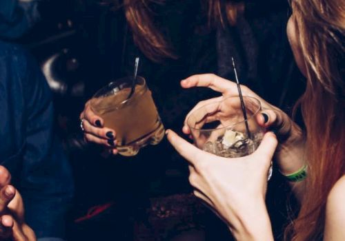 People are socializing in a lively setting, holding drinks and laughing, creating a cheerful and energetic atmosphere.