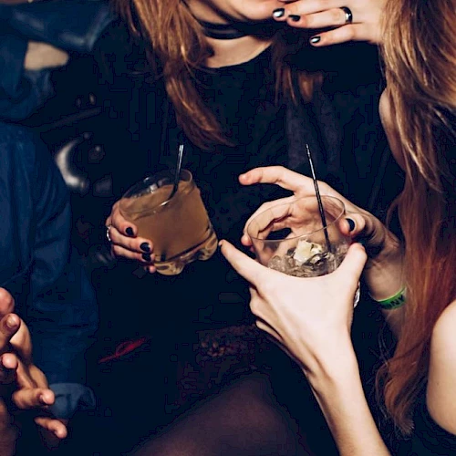 People are socializing in a lively setting, holding drinks and laughing, creating a cheerful and energetic atmosphere.