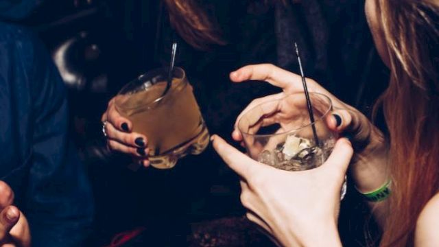 People are socializing in a lively setting, holding drinks and laughing, creating a cheerful and energetic atmosphere.