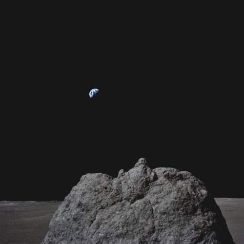 A lunar landscape with a large rock in the foreground and Earth visible in the dark sky.