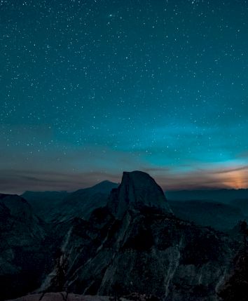 A starlit night sky over a mountainous landscape with a glowing horizon, creating a serene and captivating scene.