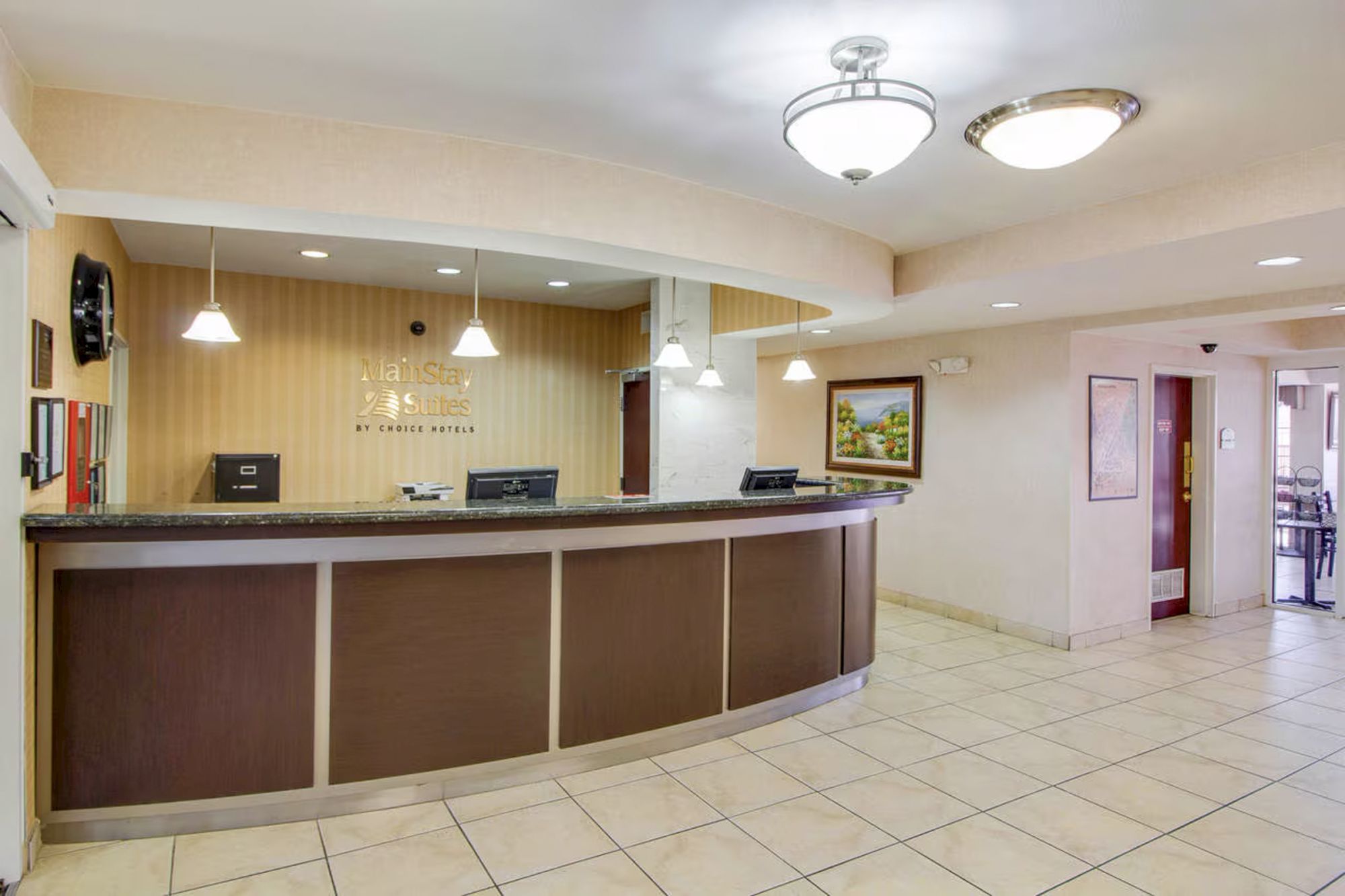 The image shows a hotel reception area with a curved desk, computers, and pendant lighting on a tiled floor with a wall sign.
