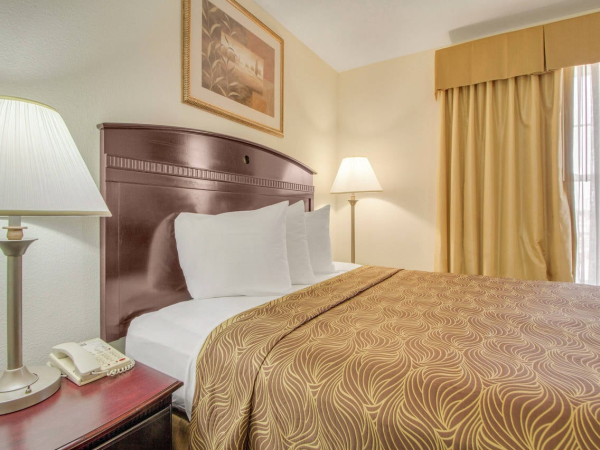 A hotel room with a bed, pillows, a patterned bedspread, two lamps, a phone, and a painting on the wall near a window.
