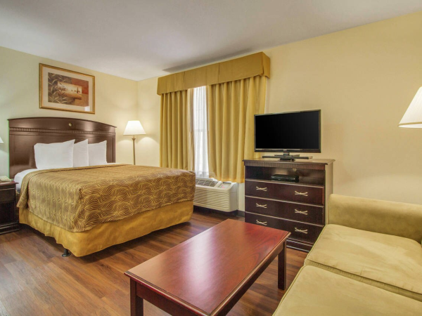 A cozy hotel room with a bed, sofa, TV, lamps, and wooden furniture, all in a warm-toned decor.