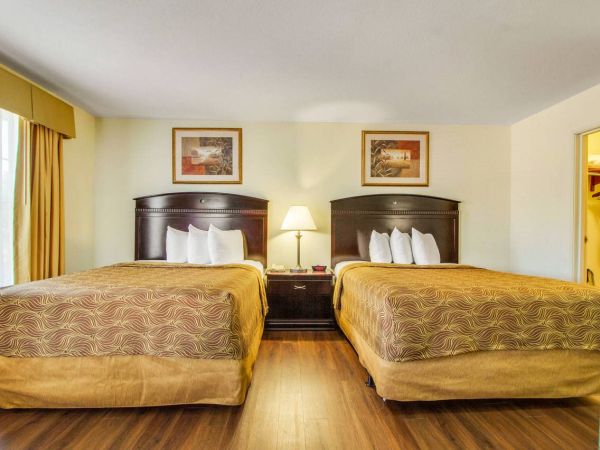 A hotel room with two beds, a nightstand, lamps, and framed art on the wall.