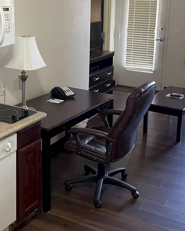 The image shows a furnished living area with a kitchenette, office chair, desk, couch, coffee table, microwave, and dishwasher.