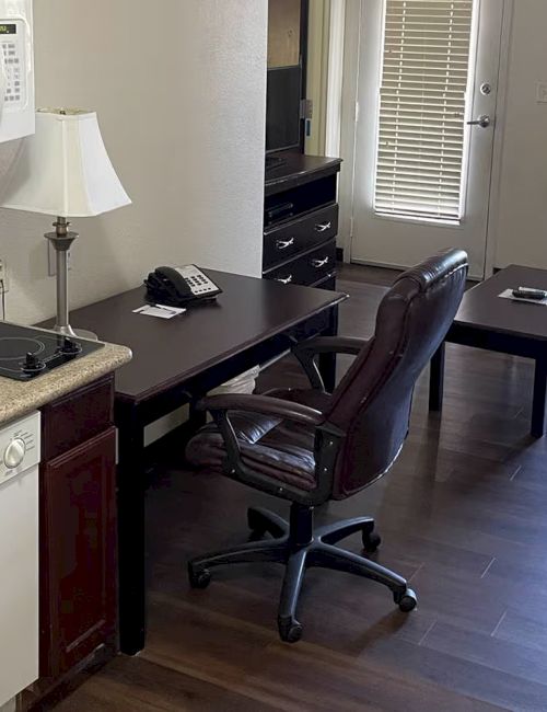 A room with kitchen appliances, desk, chair, sofa, TV, and window. Wood flooring adds a cozy touch to the compact setup.