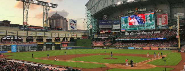 A baseball game is taking place at a stadium under a partially cloudy sky, with a large crowd and a scoreboard in the background.