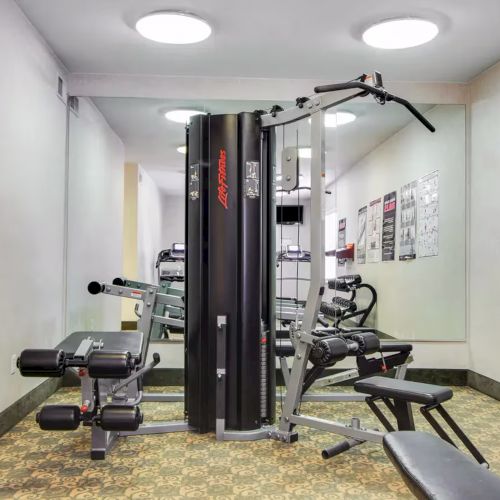 A small gym with various fitness equipment, including a multi-station machine, bench, and wall charts for exercises.