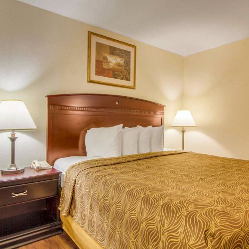 A neatly made bed with patterned linens, two bedside tables with lamps, and a framed picture on a beige wall in a cozy room.