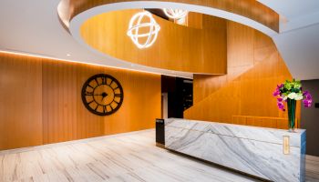 A modern reception area with a marble desk, wooden wall, clock, spiral ceiling design, and a vase of vibrant flowers on the counter.