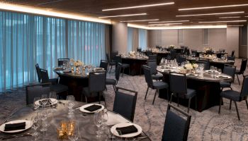 A banquet hall is set up with round tables, chairs, and elegant table settings, ready for an event.