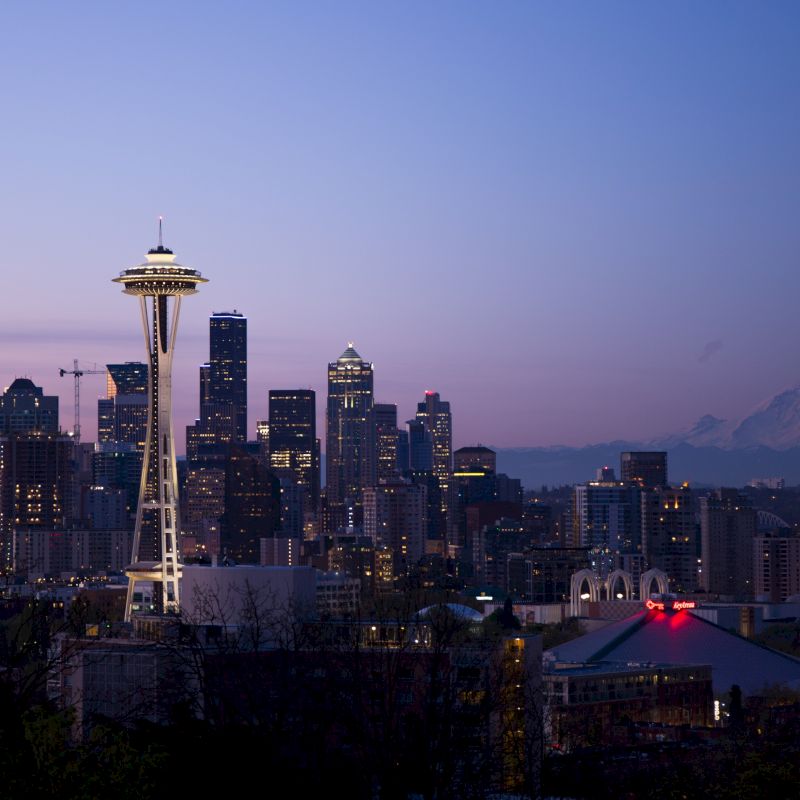 Seattle skyline at dusk with the Space Needle prominently featured and Mount Rainier visible in the background.