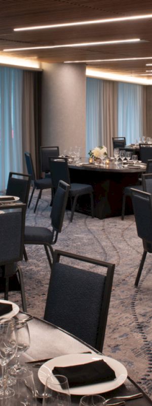 The image shows a decorated banquet hall with round tables, set with chairs, plates, glasses, and floral centerpieces, ready for an event.