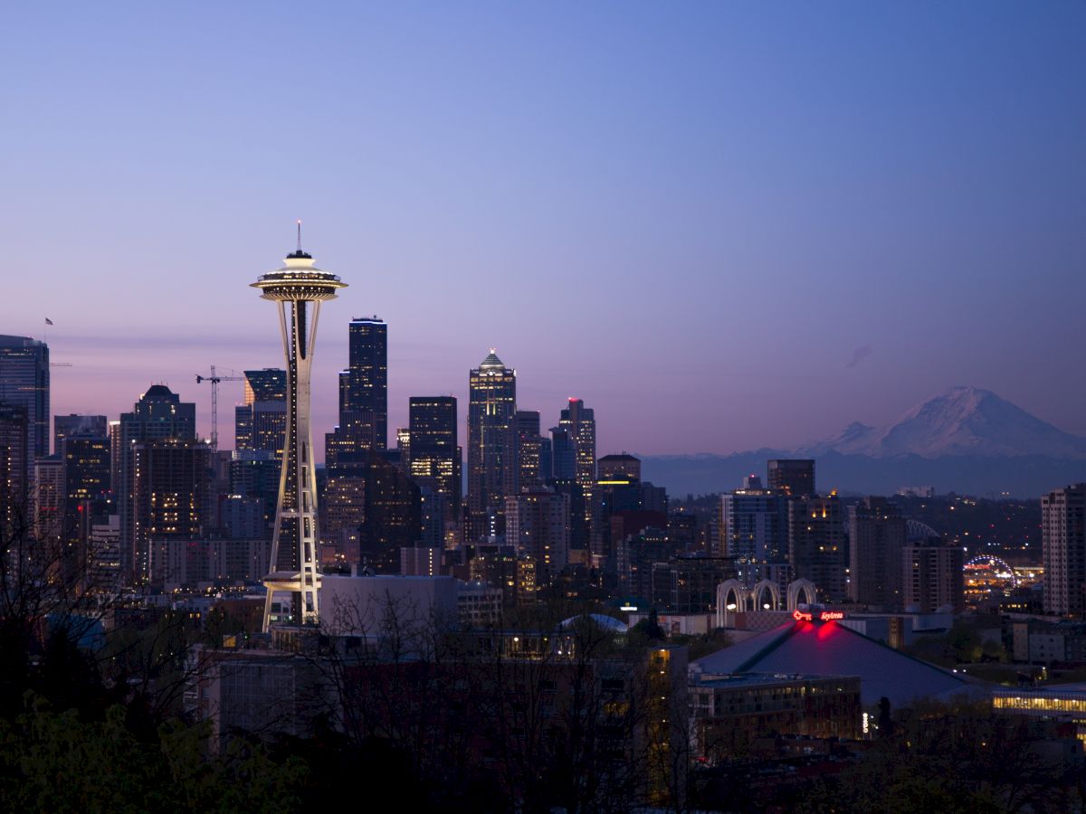 Seattle skyline at dusk, featuring the Space Needle and city buildings, with a mountain visible in the background.
