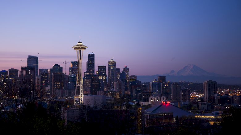 Seattle skyline at dusk, featuring the Space Needle and city buildings, with a mountain visible in the background.