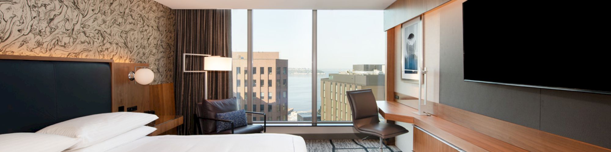 A modern hotel room features a large bed, flat-screen TV, desk, and window with city view, offering a comfortable and stylish ambiance.