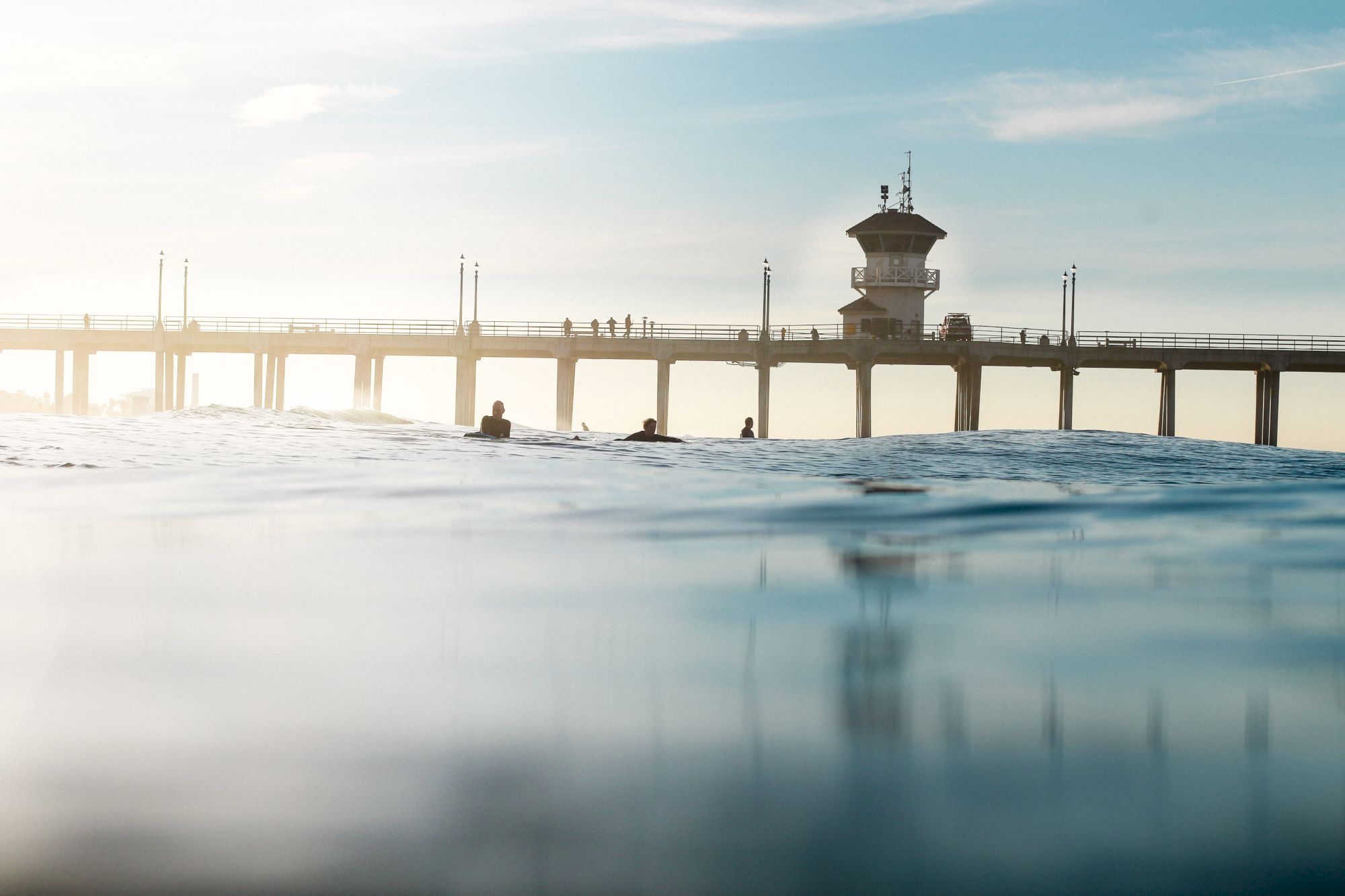 The image shows a pier with a tower structure, extending over calm water, under a clear sky with scattered clouds.